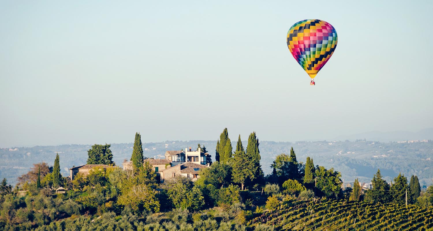 A beautiful Tuscan scene of a hot air ballon floating over a villa